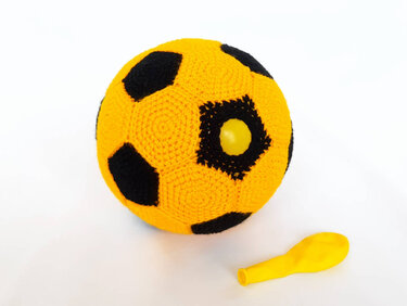 Gehäkelter gelb-schwarzer Ball mit unaufgeblasenem gelben Ballon daneben