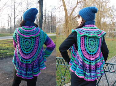Frau von hinten in bunter gehäkelter Jacke mit rundem Rückenmuster und blauer Mütze im Park