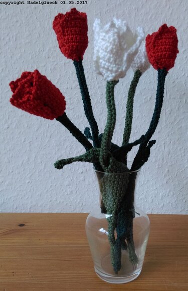 Fünf gehäkelte Tulpen (drei rot, zwei weiß) in einer klaren Glasvase auf einer Holzoberfläche