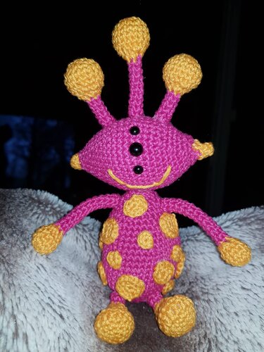 gehäkeltes Amigurumi‑Alien in Pink und Gelb mit drei Antennen und schwarzen Perlenaugen