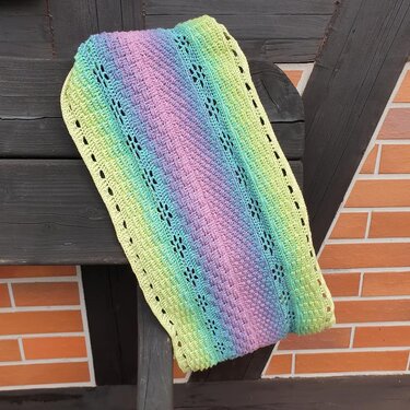 Gehäkelter Loop in Pastellfarben (Gelb, Grün, Blau, Rosa) mit Lochblütenmuster, über eine Holzleiste gelegt