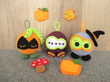 Drei gehäkelte runde Halloween Anhänger mit Schlaufen, Kürbis-Motiv, gestreiften Beinen und Hexenhut vor Holzgrund