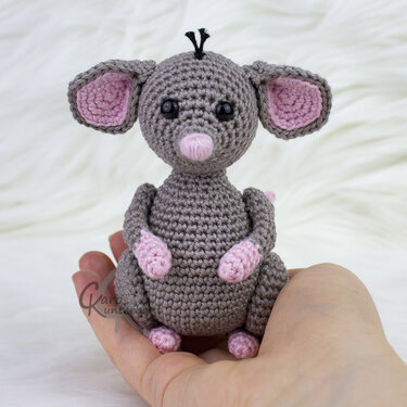 Handgehäkelte graue Amigurumi‑Maus mit rosa Ohren und Nase, gehalten in einer Hand
