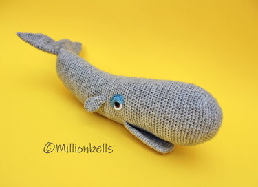 Gray crocheted amigurumi whale lying on a yellow background