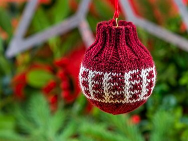 rote handgestrickte Weihnachtskugel mit weißem Muster, aufgehängt vor grünem Hintergrund
