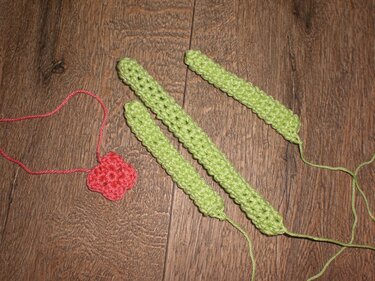 Rote Häkelblume und drei grüne gehäkelte Streifen auf Holz