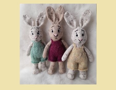 Drei gestrickte Amigurumi-Hasen mit sichtbaren Maschen und einfachen Stramplern