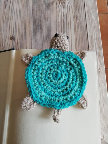 Gehäkeltes Schildkröten-Lesezeichen mit türkis-grünem Spiralpanzer auf offener Buchseite