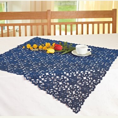 Dunkelblauer gehäkelter Tischläufer mit Blumenmuster auf weißem Tisch, dekoriert mit Blumen und einer Tasse