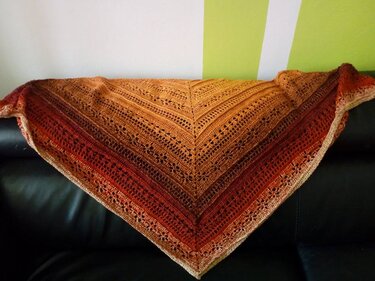 Gehäkeltes Dreieckstuch mit Farbverlauf von Gelb über Orange bis Rot, drapiert auf dunklem Sofa