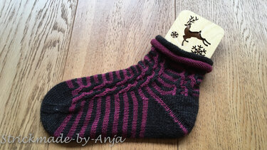 Gestrickte Damen-Socke in Dunkelgrau und Magenta mit Streifen- und Zopfmuster auf Holzboden
