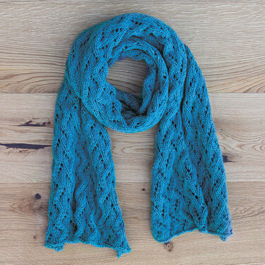 Türkisfarbener Strickschal mit filigranem Lochmuster auf Holz