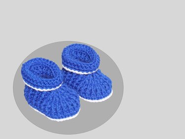 Pair of small blue crocheted baby booties with white trim on a neutral background