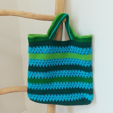 Gehäkelte Henkeltasche in Blau und Grün mit Streifenmuster, an einer Holzleiter hängend