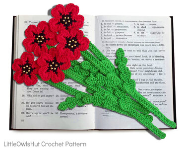 Close-up of floral crochet bookmarks with green leaf stems and beaded centers on an open book