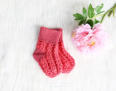 Korallrosa gehäkelte Babysocken mit Rippbündchen und Ajourmuster auf weißem Fell