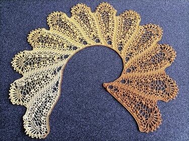 Yellow-to-amber ombre crescent crochet lace shawl laid flat on dark gray background