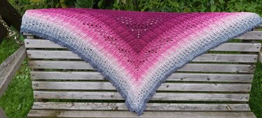 Gehäkeltes Dreieckstuch mit Ombre-Farbverlauf (Magenta–Rosa–Grau) auf einer Holzbank