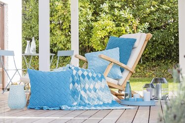 Holzliege auf Terrasse mit hellblauem gestricktem Kissen, kariertem Plaid und Tablett mit Kerzen