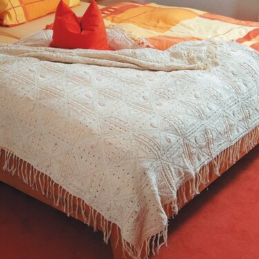 Hellbeige gehäkelte Tagesdecke mit Fransen auf einem Bett mit orange-gelber Bettwäsche