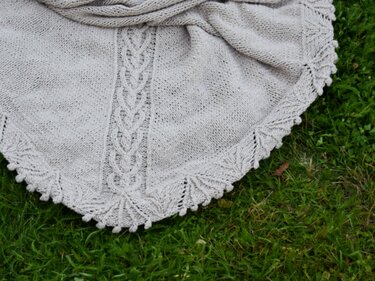 Hellbeiges gestricktes Dreieckstuch mit mittigem Zopfmuster und gezacktem Spitzensaum auf Gras