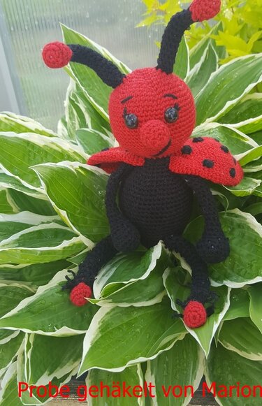 Handgehäkelter roter Marienkäfer-Amigurumi mit schwarzen Punkten auf grün-weiß gerandeten Blättern