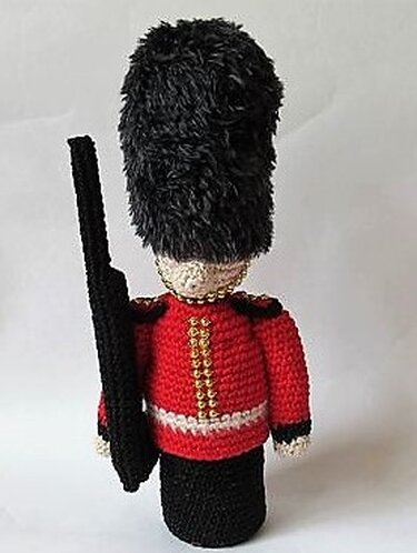 Gehäkelte Wachsoldatenpuppe in rotem Jackett, hoher schwarzer Bärenfellmütze und mit Spielzeuggewehr