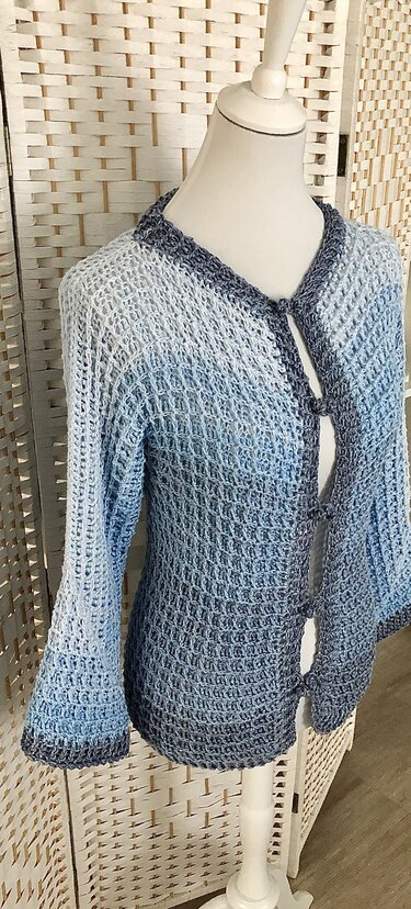 Gehäkelte Damenjacke in Blau-Ombré auf Schneiderpuppe, offenes Maschenbild und drei Schlaufenverschlüsse