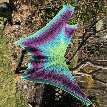 Gehäkeltes Dreieckstuch mit Farbverlauf in Grün, Türkis und Lila, aufgehängt im Garten