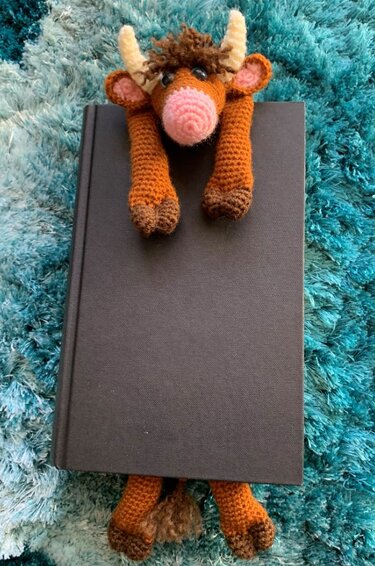 Brown crocheted amigurumi bull bookmark draped over a black hardcover book