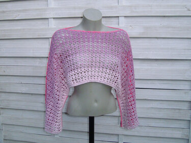 Gehäkelter rosa Bolero mit Lochmuster auf Schaufensterpuppe vor weißer Holzfassade.