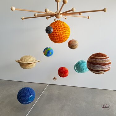 Holzmobile mit gehäkelten Kugeln, die Sonne und Planeten des Sonnensystems darstellen, vor weißer Wand.