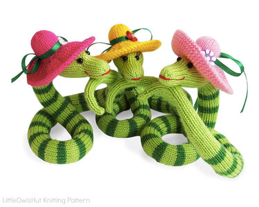 Three green striped knitted amigurumi snakes wearing colorful small hats with ribbons on a white background.