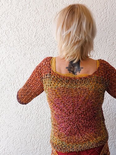 Rückenansicht einer Person, die ein mehrfarbiges, gehäkeltes Shirt mit offenem Maschenmuster trägt.