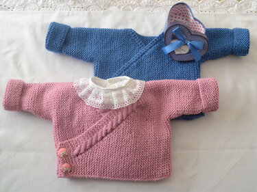 Zwei gestrickte Babyjacken liegend: rosa Wickeljacke mit Zopf und Spitzenkragen, blaue Jacke mit umgeschlagenen Bündchen