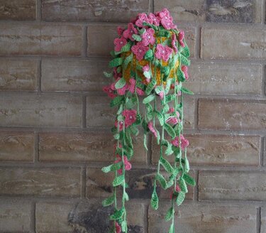 Gehäkelte Hängeampel mit langen grünen Ranken und rosa Blumen