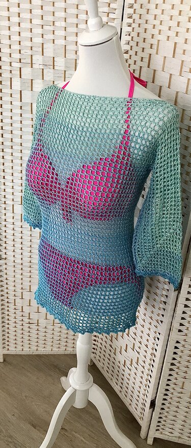Gehäkelter Netzpullover in Türkis‑Blau auf Schaufensterpuppe über rosa Bikini