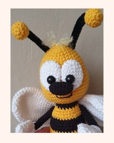 Detailansicht einer gehäkelten Amigurumi-Biene mit gelb-schwarzen Streifen und weißen Flügeln