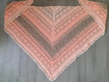 Gehäkeltes Dreieckstuch in Pfirsich-, Rosa- und Grautönen mit Spitzenmuster und Muschelrand, von oben fotografiert.