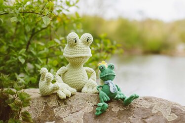Zwei gehäkelte Amigurumi-Frösche in Hellgrün und Dunkelgrün auf einem Stein am Teich