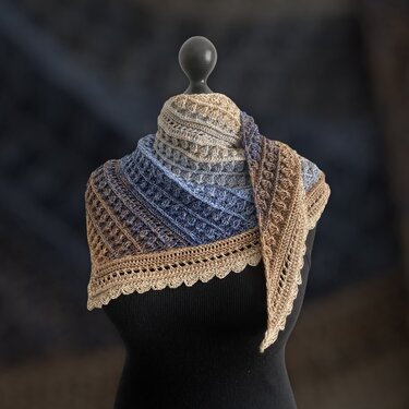 Mannequin wearing a triangle crochet shawl in beige to blue gradient with textured stitches and scalloped edge