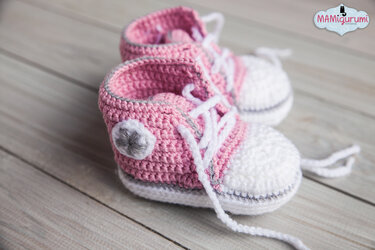 Gehäkelte rosa-weiße Babyschuhe im Sneaker-Stil mit weißen Schnürsenkeln auf Holzoberfläche