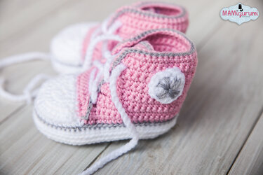 Gehäkelte Babysneaker in Rosa und Weiß mit weißen Schnürsenkeln auf heller Holzoberfläche