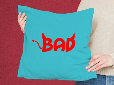 Türkisfarbenes Kissen mit rotem 'BAD'-Schriftzug im Teufelsstil