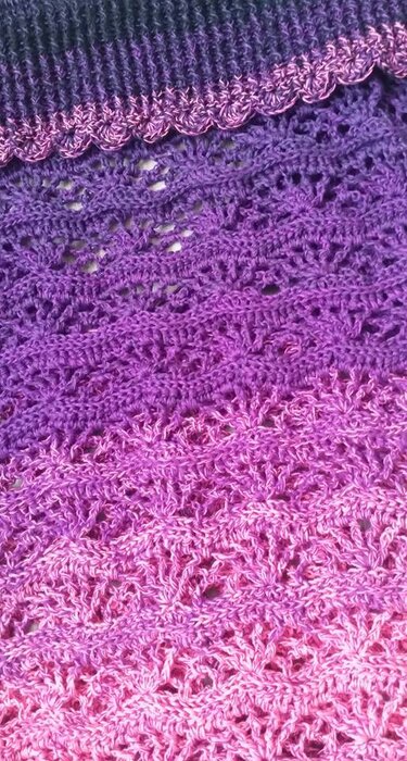 Detail einer gehäkelten Decke mit Lochmustern und Muschelrand in Rosa‑Violett