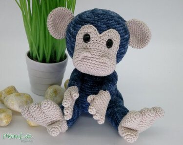 Gehäkelter Amigurumi-Affe in Blau und Beige neben einer Topfpflanze auf hellem Untergrund.