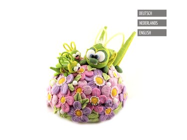 Drei gehäkelte grüne Käfer auf einem Hügel aus rosa, lila und gelben Häkelblüten mit weißen Perlen