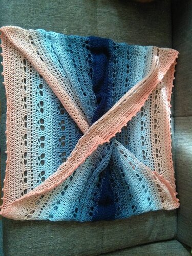 Gehäkelter Loop-Schal mit Farbverlauf von Rosa zu Blau, gefaltet auf einem Sofa, sichtbares Lochmuster