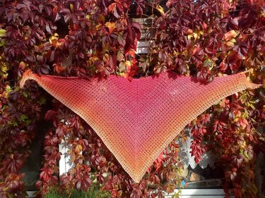 Herbstliches gehäkeltes Dreieckstuch in Rot- und Orangetönen vor roten Weinblättern
