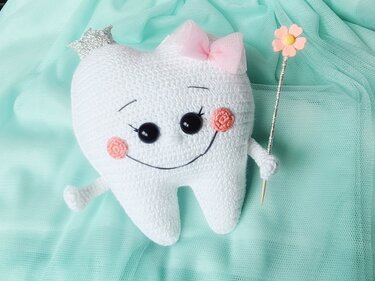 niedliches gehäkeltes Zahn-Amigurumi mit rosa Schleife, Krönchen und Blumenstab auf mintgrünem Tüll